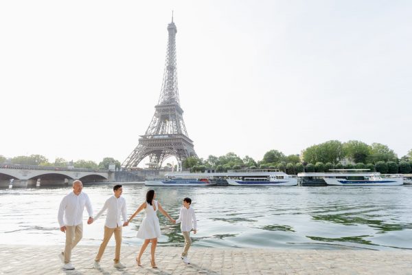 Cute family smiling and walking on the banks of the Seine in front of the Eiffel Tower during a Paris photoshoot