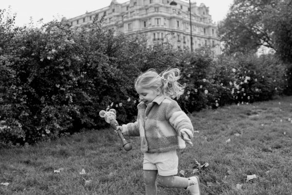 Daughter smiling and running in flower garden with Parisian building in background blowing bubbles during photoshoot