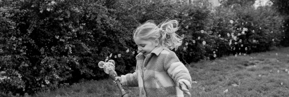 Daughter smiling and running in flower garden with Parisian building in background blowing bubbles during photoshoot