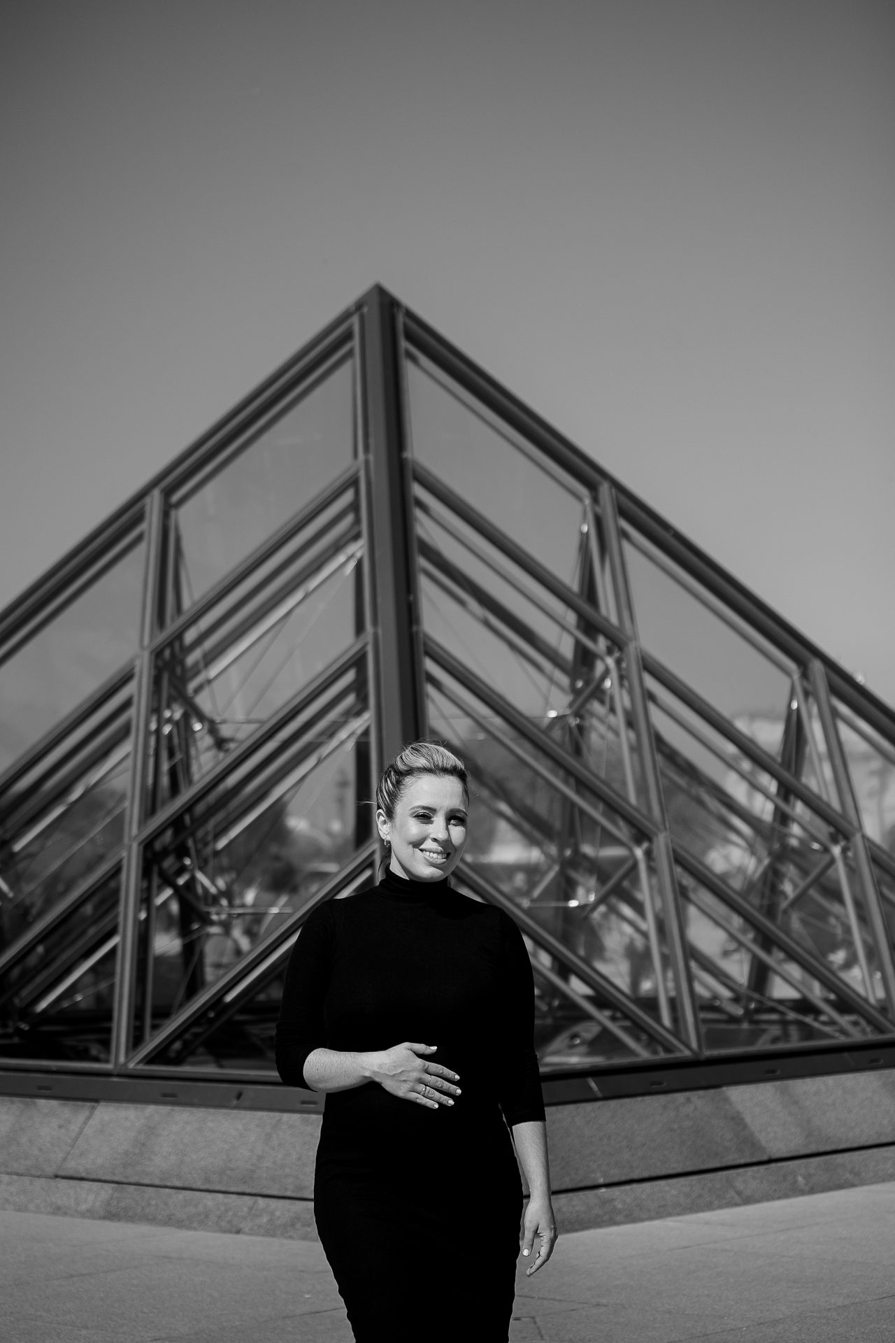Black and white photo of pregnant woman posing at Louvre Pyramids during Paris maternity photoshoot