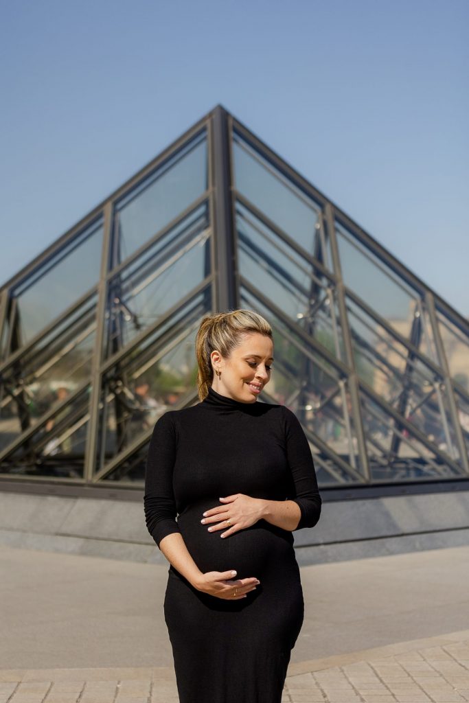 Pregnant woman posing in front of Louvre Pyramids during Paris maternity photoshoot