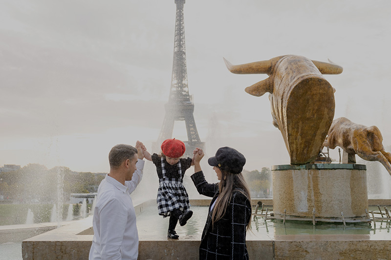 A family with a young daughter playing by a fountain at the Trocadéro in Paris, with the Eiffel Tower in the background during a family photoshoot.