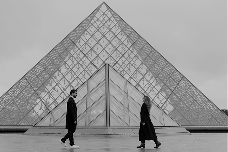 Cute couple in front of the Louvre Museum in Paris, captured in a timeless black and white photo.